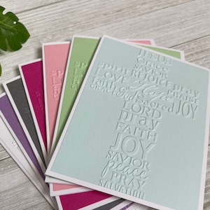 May include: A stack of blank cards with a light blue card on top. The light blue card has a cross made of embossed words, including "Jesus", "Grace", "Savior", "Love", "Rejoice", "Pray", "Praise", "Life", "Faith", "God", "Sacred", "Joy", "Lord", "Pray", "Faith", "Joy", "Savior", "Peace", "Pray", and "Salvation".