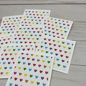 May include: A stack of white cards with a scalloped edge. Each card has a white background with a pattern of small, colorful hearts.