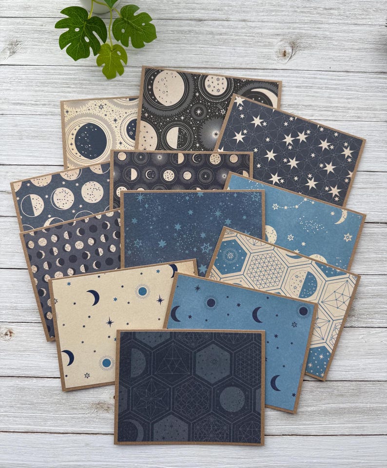 May include: A set of 10 blank note cards featuring different celestial patterns in shades of blue and cream. The patterns include moons, stars, and geometric designs.