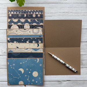 May include: A set of 10 blank note cards featuring blue and white celestial patterns. The cards are made from brown cardstock and come with a kraft paper envelope.