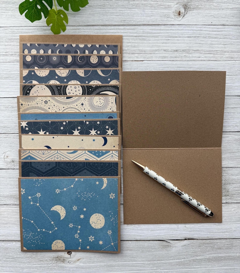 May include: A set of 10 blank note cards featuring blue and white celestial patterns. The cards are made from brown cardstock and come with a kraft paper envelope.