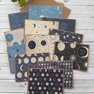 May include: A set of 10 celestial-themed note cards with envelopes. The cards feature various patterns of moons, stars, and constellations in shades of blue, black, and white.