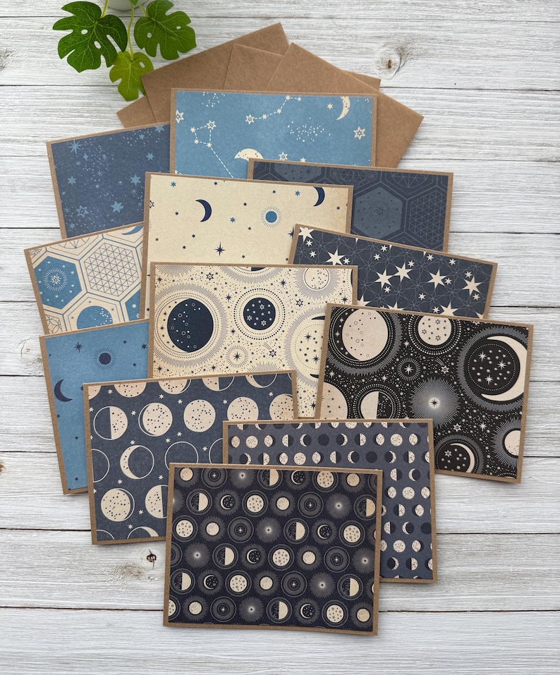 May include: A set of 10 celestial-themed note cards with envelopes. The cards feature various patterns of moons, stars, and constellations in shades of blue, black, and white.