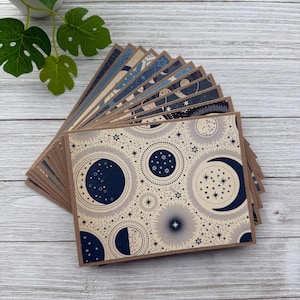 May include: A stack of blank note cards with a celestial design featuring moons, stars, and a navy blue and cream colour scheme.
