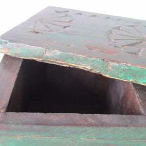 Puede incluir: Caja de madera antigua parcialmente abierta, con acabado turquesa desgastado. La tapa presenta dise&ntilde;os florales tallados. El interior es oscuro, revelando compartimentos. Probablemente utilizada para almacenamiento o exhibici&oacute;n.