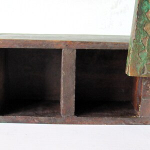 Puede incluir: Una caja de madera marr&oacute;n oscuro con dos compartimentos. La caja tiene forma rectangular y parece hecha a mano. Un elemento decorativo verde y bronceado est&aacute; unido al lateral, con dise&ntilde;os florales y geom&eacute;tricos.