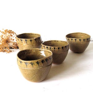 May include: A set of four speckled tan ceramic bowls with a rounded shape. Each bowl features a dark blue hand-painted floral pattern around the rim and a subtle textured leaf-like impression on the lower exterior surface of the clay body.