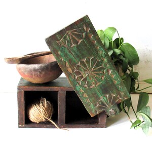 Puede incluir: Una caja de madera r&uacute;stica con dos compartimentos, uno con una madeja de hilo. Un panel de madera tallada y pintada de verde con dise&ntilde;os geom&eacute;tricos se apoya en la caja. Un cuenco y una cuchara de madera est&aacute;n cerca.