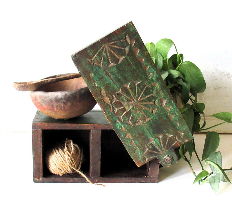 Puede incluir: Una caja de madera r&uacute;stica con dos compartimentos, uno con una madeja de hilo. Un panel de madera tallada y pintada de verde con dise&ntilde;os geom&eacute;tricos se apoya en la caja. Un cuenco y una cuchara de madera est&aacute;n cerca.