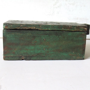 Puede incluir: Una caja rectangular de madera con tapa con bisagras. La caja est&aacute; pintada en un color verde desgastado, con vetas de madera visibles y signos de desgaste. La caja parece ser vintage o antigua.
