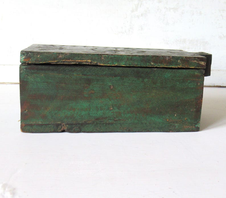 Puede incluir: Una caja rectangular de madera con tapa con bisagras. La caja est&aacute; pintada en un color verde desgastado, con vetas de madera visibles y signos de desgaste. La caja parece ser vintage o antigua.