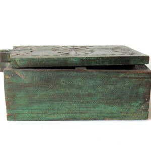 Puede incluir: Caja rectangular de madera de estilo antiguo con tapa con bisagras. La caja est&aacute; pintada en un color verde desgastado, con vetas de madera visibles. La tapa presenta dise&ntilde;os florales tallados. La caja est&aacute; abierta.