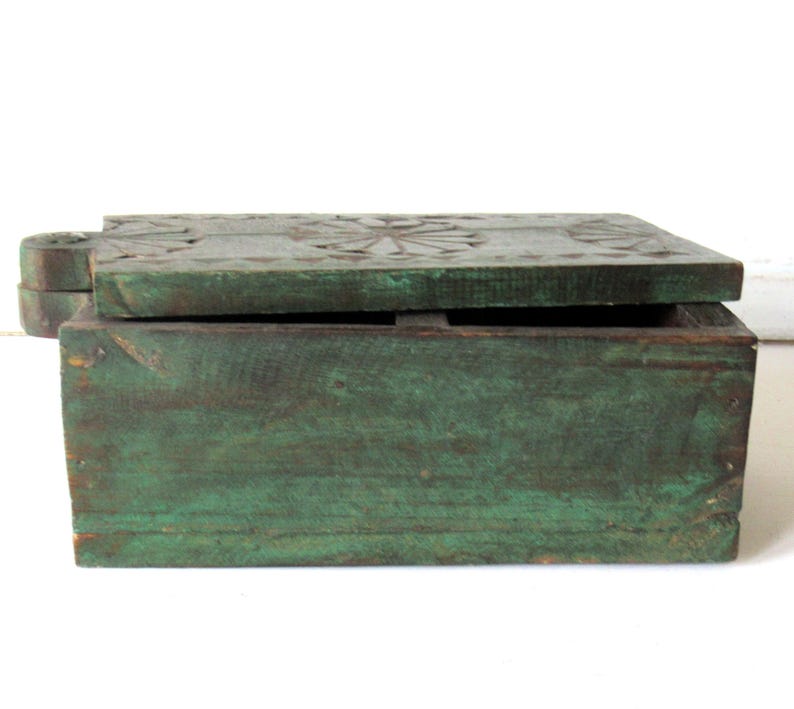 Puede incluir: Caja rectangular de madera de estilo antiguo con tapa con bisagras. La caja est&aacute; pintada en un color verde desgastado, con vetas de madera visibles. La tapa presenta dise&ntilde;os florales tallados. La caja est&aacute; abierta.