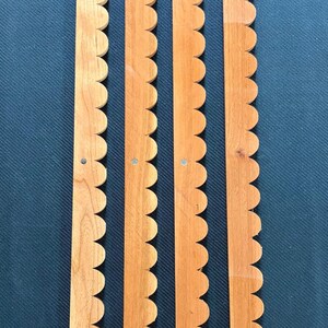 Peut inclure: Quatre longues bandes de bois &eacute;troites avec un bord festonn&eacute; sur un c&ocirc;t&eacute;. Chaque bande pr&eacute;sente une finition en grain de bois brun clair et comprend trois petites attaches m&eacute;talliques circulaires ou trous de vis espac&eacute;s r&eacute;guli&egrave;rement.