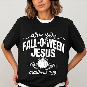 Può includere: Una t-shirt nera a maniche corte con testo bianco che recita are you FALL-O-WEEN JESUS, un disegno di una zucca e il testo matthew 4:19. La maglietta presenta un girocollo e una vestibilità standard, con la grafica centrata sul petto.