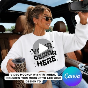 May include: A white crewneck sweatshirt featuring a central gray circle graphic with the black text "YOUR DESIGN HERE" surrounded by small heart and star icons. The sweatshirt is worn with blue jeans and held with a leopard print tumbler.
