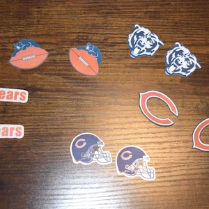 Puede incluir: Una colección de pegatinas con temática de los Chicago Bears que incluye dos balones de fútbol americano con logos de osos, dos logos de cabezas de oso, dos logos C en naranja y azul marino, dos cascos con logos C y dos pegatinas con Da Bears.