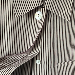 May include: A button-down shirt featuring a vertical striped pattern in dark maroon and off-white. The garment includes a pointed collar, two iridescent mother-of-pearl buttons, and a small patch pocket on the lower right side. A care label is visible.