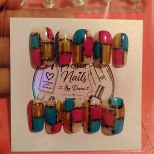 May include: A set of ten press-on nails featuring a patchwork design with alternating squares of bright pink, teal, and metallic gold, accented by black stitched lines. The nails are displayed on a white card labeled Pressed Nails By Dasia.