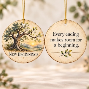 May include: Two round ceramic ornaments with gold hanging strings. One features a tree at sunset with the text New Beginnings. The other displays the text Every ending makes room for a beginning with a small green leaf illustration.