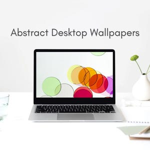 May include: A silver laptop displaying a screen with overlapping colorful circles in yellow, orange, red, pink, and green. Above the laptop, the text reads Abstract Desktop Wallpapers. A clear glass of water and a white vase with green flowers are present.