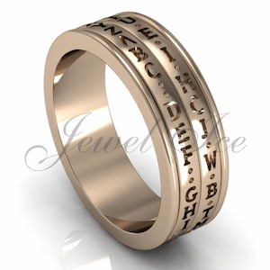 May include: A rose gold-toned ring featuring a wide band with two recessed channels. The channels are engraved with a sequence of uppercase letters of the alphabet, separated by small dots, encircling the entire outer circumference of the ring.