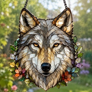 Könnte beinhalten: Ein Buntglas-Sonnenfänger in Form eines Wolfskopfes, bestehend aus grauen, weißen und beigen Glaselementen. Der Wolf hat leuchtend bernsteinfarbene Augen und eine schwarze Nase, umrahmt von einer Bordüre aus bunten Glasblättern und Blüten.