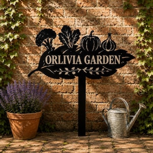 以下が含まれることがあります： ORLIVIA GARDENという文字が刻まれた葉の形の看板が付いた黒い金属製のガーデンステーク。ブロッコリー、葉物野菜、カボチャ、ニンニクの球根のシルエットがデザインされており、垂直の支柱に取り付けられています。