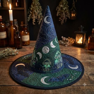 May include: A quilted pointed hat featuring a dark blue and green color scheme with embroidered silver moon phases, mushrooms, and bats. The fabric displays intricate swirling stitch patterns throughout the conical shape and wide brim.