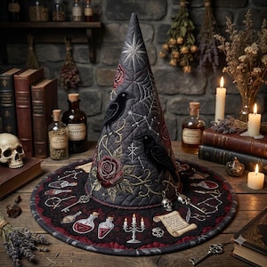 May include: A quilted gray witch hat featuring embroidered black ravens, red roses, spiderwebs, and celestial patterns. The wide brim is decorated with embroidered potion bottles, keys, skulls, a candelabra, and a scroll, finished with dangling charms.
