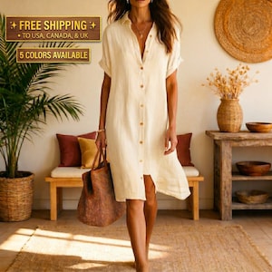 May include: A knee-length, cream-coloured button-down shirt dress with short sleeves, a classic collar, and a straight hemline. The garment is made of a textured fabric and is paired with a large, brown, woven tote bag held at the side.