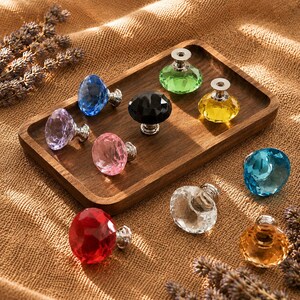 May include: A collection of faceted, diamond-shaped cabinet knobs in various colors including red, blue, yellow, green, black, pink, purple, clear, and amber. Each knob features a polished silver-tone metal base and a multi-faceted glass top.