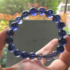 Puede incluir: Una pulsera circular compuesta por cuentas lisas, redondas y translúcidas en tonos variados de violeta intenso y azul añil. Las cuentas están ensartadas en un cordón flexible, creando un bucle continuo de elementos esféricos pulidos.
