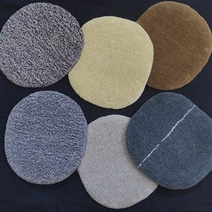 May include: Six round, fluffy rugs in various colors and textures. The rugs are arranged in a circle on a black surface. The colors include gray, beige, brown, and cream.