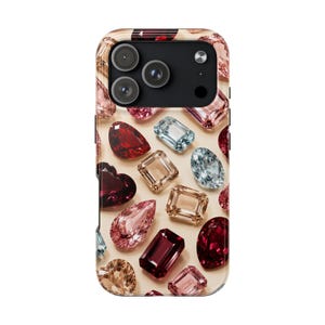 May include: A smartphone case featuring a pattern of various faceted gemstones in shades of deep red, light pink, peach, and pale blue. The design includes pear, oval, heart, and rectangular cut jewels arranged against a light beige background.