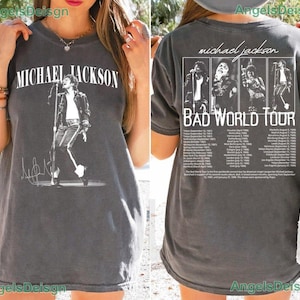 May include: A charcoal gray short-sleeve t-shirt featuring a white graphic of Michael Jackson on the front and a Bad World Tour graphic on the back, including four black and white photos of the artist and a list of tour dates and locations.