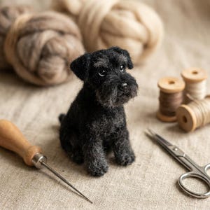 Op de afbeelding: Een klein, naaldgevilte zwart hondje met een textuurrijke vacht, donkere ogen en een opvallende snuit. Het miniatuurbeeldje staat tussen knutselbenodigdheden, waaronder houten garenklosjes, een metalen schaar en een priem.