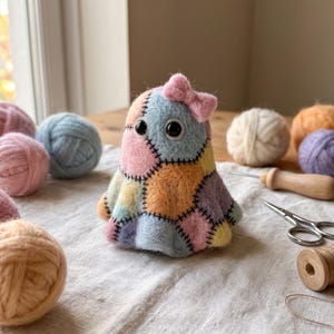May include: A needle-felted ghost figurine crafted from multi-colored pastel wool patches in shades of pink, blue, yellow, and purple. The ghost features black bead eyes, a small pink felt bow on top, and visible black stitched seams.