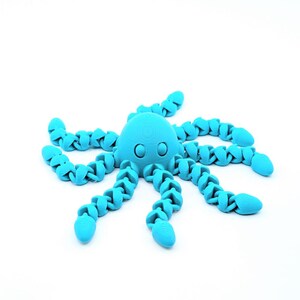 May include: A bright cyan articulated octopus figurine featuring a smooth, rounded head with two circular eyes and eight segmented, flexible tentacles extending outward in a radial pattern, showcasing a 3D printed texture throughout the surface.