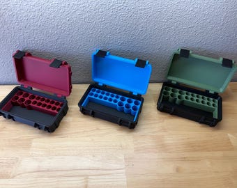 May include: Three rectangular storage cases with black outer shells and hinged lids. Each case features a colored interior insert with multiple circular cutouts for organization. The inserts are available in matte red, bright blue, and olive green.