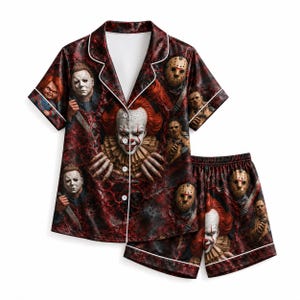 May include: A short-sleeve button-down pyjama shirt and matching shorts set featuring a dark red, textured background with a collage of horror movie characters including a clown, masked figures, and a doll, all accented with white piping trim.