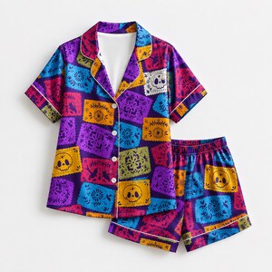 May include: A short-sleeve button-down pajama shirt and matching shorts set featuring a vibrant, multi-colored pattern of rectangular panels with floral designs and skull motifs in shades of purple, blue, yellow, and orange with white piping.