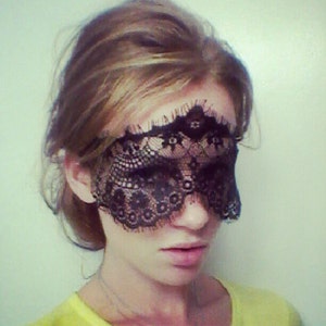 May include: A woman wearing a black lace eye mask. The mask is delicate and intricate, with a floral pattern.