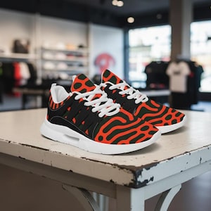 May include: A pair of athletic sneakers featuring a vibrant orange and black organic, wavy pattern across the upper fabric. The shoes include white laces, a white interior lining, and a thick, solid white rubber sole for support and cushioning.