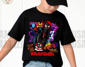 May include: A black short-sleeved t-shirt featuring a graphic of a masked character in a red hoodie, white trainers, and black trousers. The design includes colourful graffiti-style elements, the number 7, and the name BRANDON in red letters.