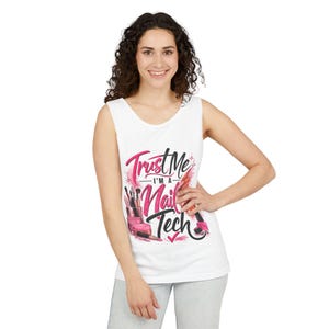 May include: A white sleeveless tank top featuring a graphic print with the text Trust Me I'M A Nail Tech in pink and black lettering. The design includes illustrations of various nail polish bottles, makeup brushes, and cosmetic tools in pink tones.