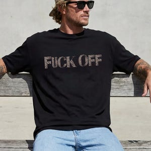 Könnte beinhalten: Ein schwarzes kurzärmeliges T-Shirt mit dem Text FUCK OFF in einem braun-schwarzen Leopardenmuster auf der Brust. Das Shirt hat einen Rundhalsausschnitt und eine Standardpassform aus einfarbigem schwarzem Stoff.