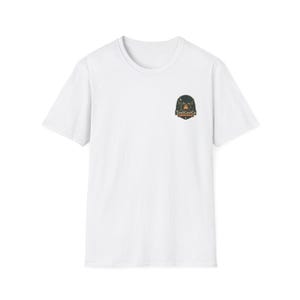 Puede incluir: Una camiseta blanca de manga corta con un pequeño logotipo centrado en el pecho. El logotipo es un emblema oscuro en forma de escudo que representa una escena forestal con una luna creciente y el texto TrailCastCo impreso en blanco y naranja.
