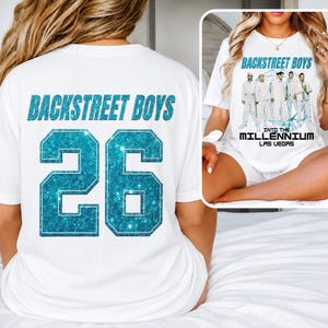 Könnte beinhalten: Ein weißes T-Shirt mit dem Schriftzug BACKSTREET BOYS und der Zahl 26 in glitzerndem Blau auf der Rückseite. Die Vorderseite zeigt eine Grafik der Bandmitglieder mit dem Text BACKSTREET BOYS INTO THE MILLENNIUM LAS VEGAS.