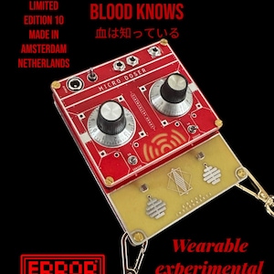 Puede incluir: Un sintetizador experimental portátil rojo y dorado llamado "Micro Doser Blood Knows" con el texto "血は知っている" en japonés. El sintetizador tiene dos botones y un interruptor. Está hecho por Error Instruments.